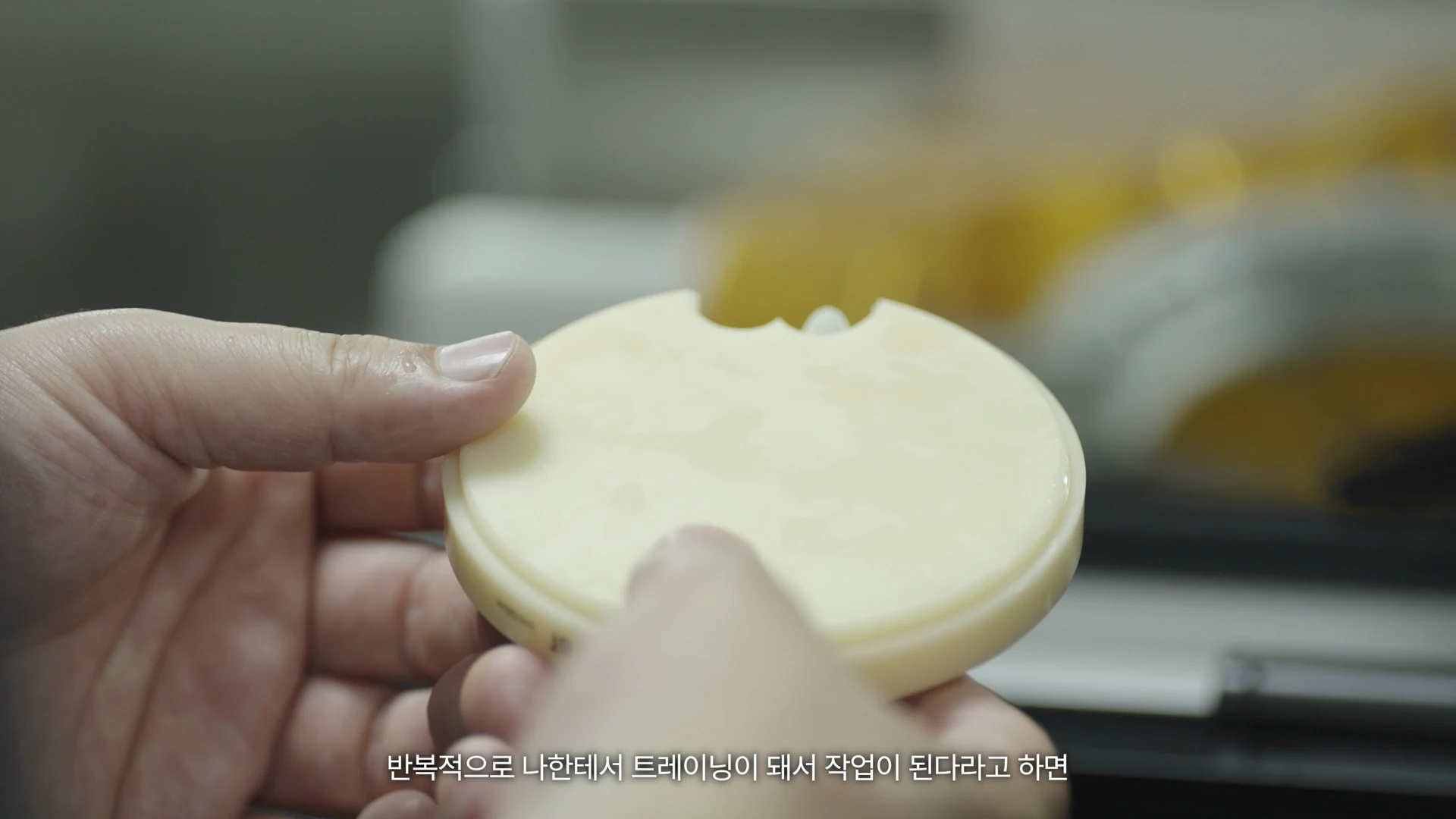 The laboratory lead’s hands holding and examining a small round holder