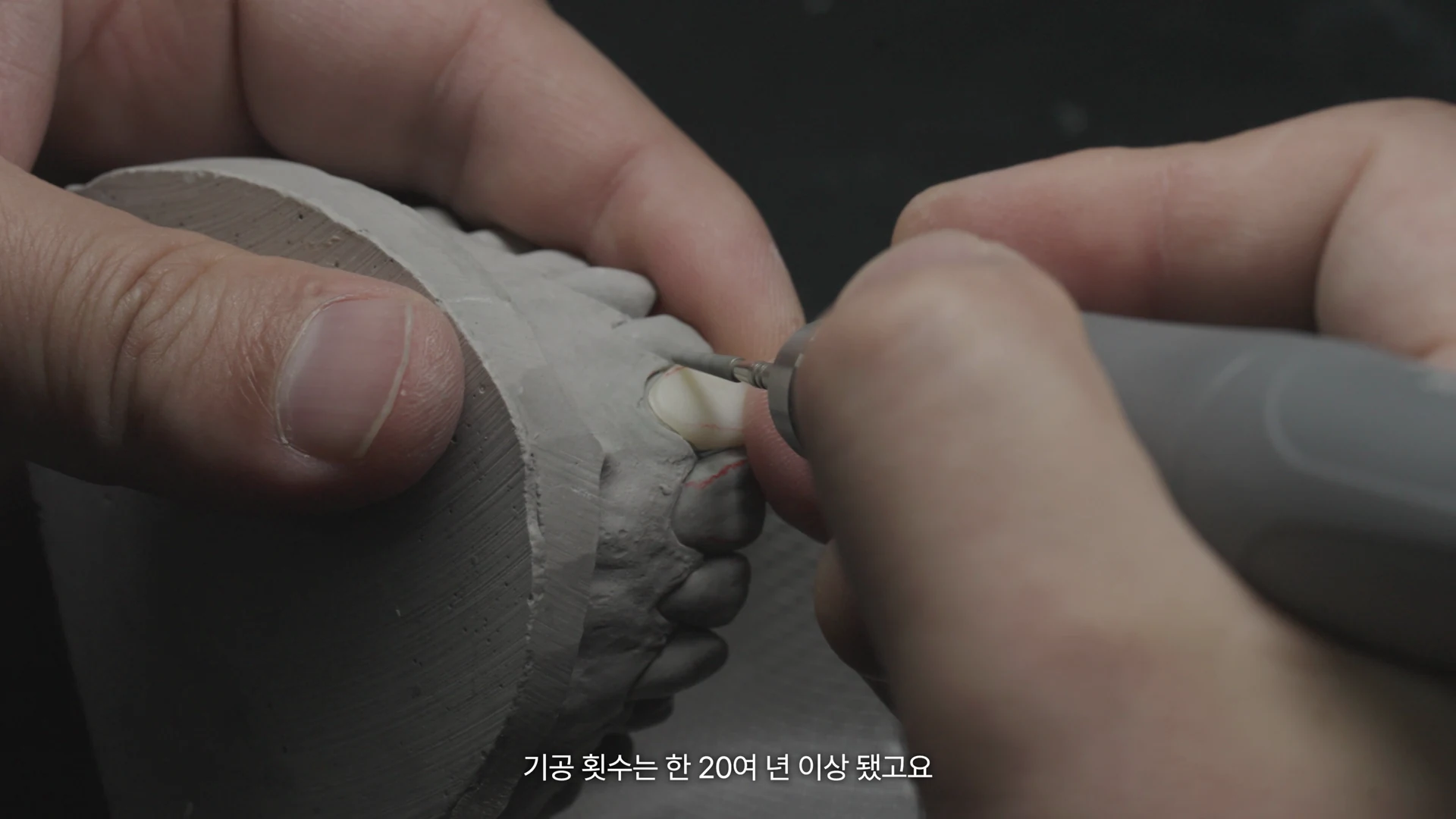The laboratory director holds a piece while shaping it with a rotary tool